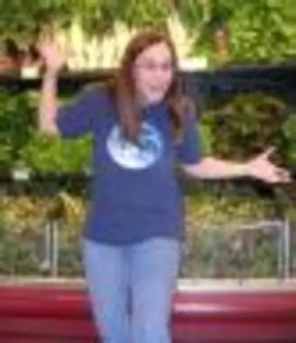 Woman in blue shirt standing outdoors with arms outstretched