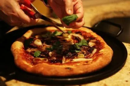 Person garnishing a fresh vegetarian pizza with basil on a dark plate