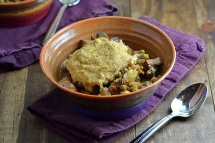 Vegetable pot pie with cornbread topping in a ceramic bowl on purple napkin