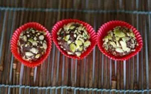 Three vegan chocolate truffles topped with sliced pistachios in red paper cups