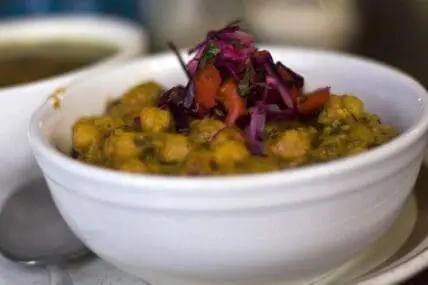 Vegan chickpea curry garnished with purple cabbage and herbs in a white bowl