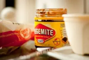 A jar of Vegemite spread next to a red tube of toothpaste on a bathroom counter.