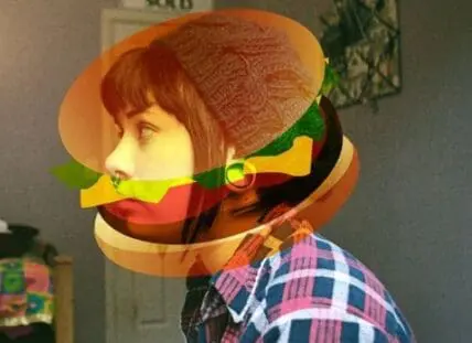 Person wearing a large hamburger bun costume head with colorful striped shirt