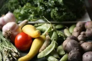 Fresh vegetables including garlic, tomato, yellow squash, peas, kale, and beets