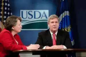 Two officials at a table with USDA logo and American flag in background