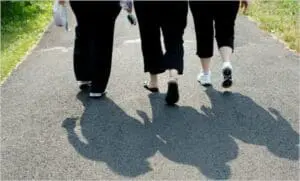 Three people walking together on a paved path, casting shadows on the ground.