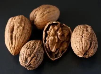 Six whole and cracked walnuts on a dark background