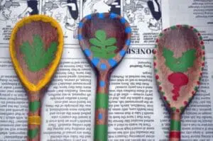 Three handmade garden plant markers with green leaf designs on wooden spoons with colored borders