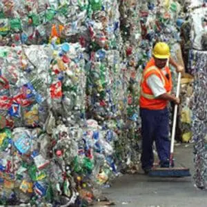 Worker in safety gear organizing stacked bundles of compressed plastic bottles at recycling facility