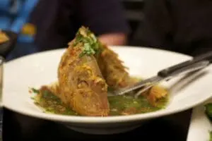 Crispy fried food triangle topped with green sauce on white plate