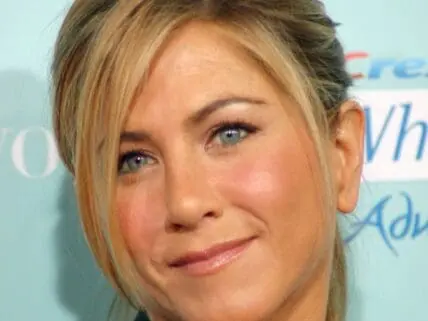 Jennifer Aniston at a media event wearing blonde hair and a subtle smile