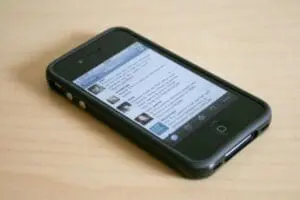 Black iPhone displaying a social media feed on wooden surface