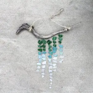 Handmade wind chime with curved driftwood, string, and cascading green and blue sea glass pieces