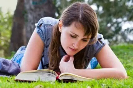 Young woman reading a book while lying on grass outdoors