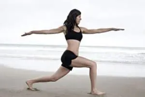 Woman performing a warrior pose yoga position on a beach