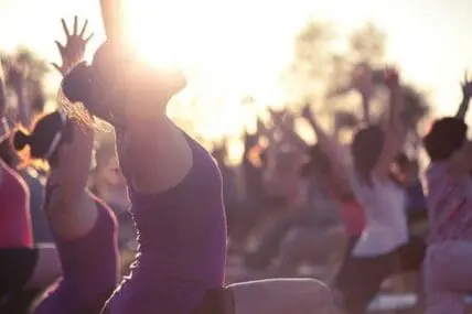 Group of people practicing yoga outdoors at sunset with hands raised