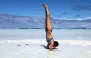 Man performing a headstand in shallow ocean water at a tropical beach