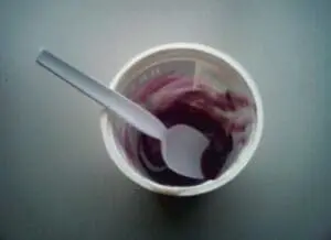White yogurt cup with purple yogurt and a spoon inside