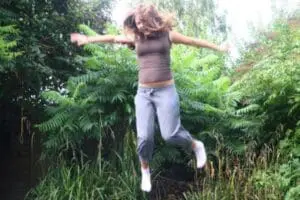 Woman jumping outdoors with arms outstretched in a grassy garden setting