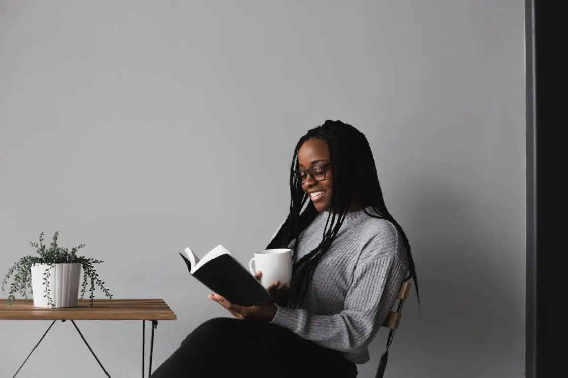 Image: woman reading drinking coffee while reading a book.  vegan collagen supplement powders may help the body's own collagen production.
