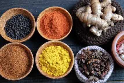 image of ground spices such as turmeric and ginger, whole peppercorns and star anise, and ginger whole all in small wooden bowls with dark wood background for Ayurveda cleanse