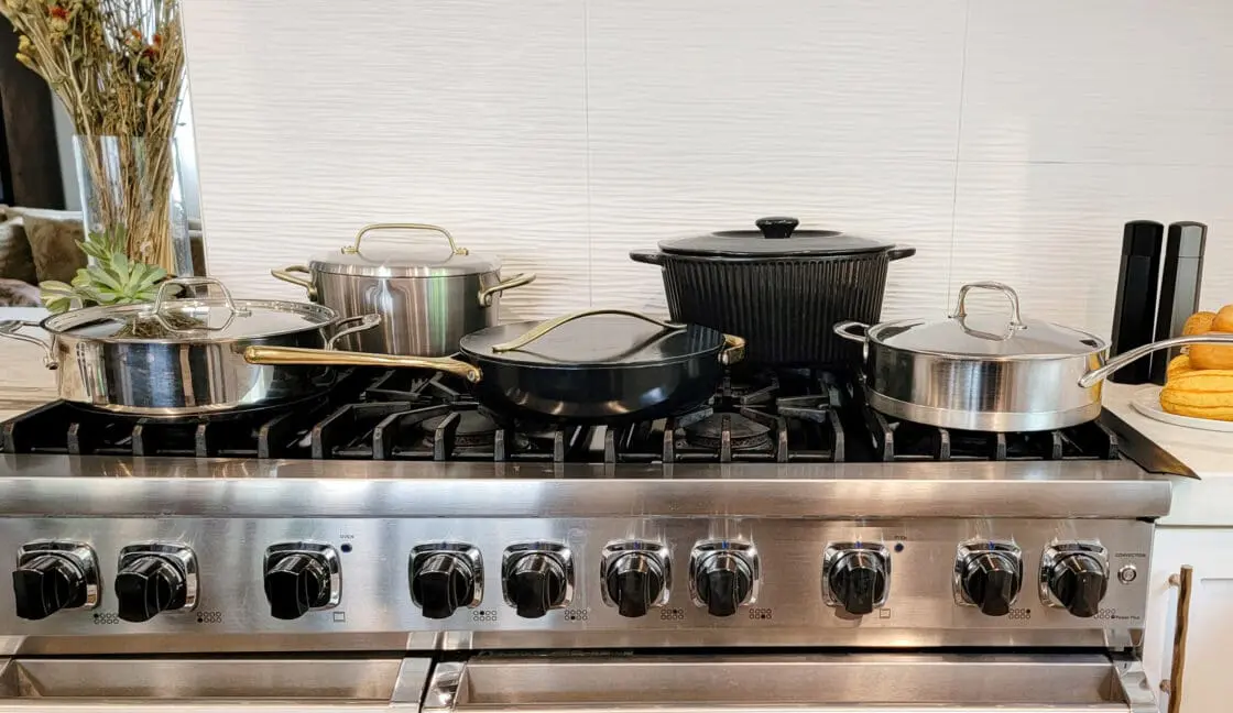 Image of Caraway cookware and more brands on Laura Klein's professional stovetop. brands include Alva Cookware, GreenPan, Caraway, Xtrema, Staub, Made In, and Demeyere cookware including ceramic coated non stick cookware