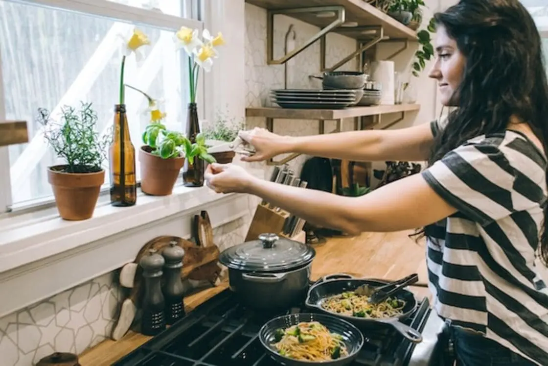 woman trimming basil in her kitchen leaning over her safe cast iron cookware. We don't recommend The Always Pan because it deteriorates too quickly and ends up in the trash. Glass cookware and porcelain enamel can be excellent choices too. We help you choose the right types of cookware.