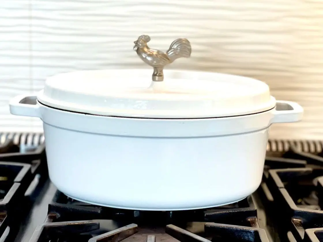 Image of Laura Klein's Staub white oval cocotte on gas stove top makes naturally non stick cooking a breeze. Staub's Dutch Ovens are free of toxic metals and have a textured surface and is metal utensil safe that is excellent for searing. It is an excellent piece of cookware and should be part of your non toxic cookware sets 