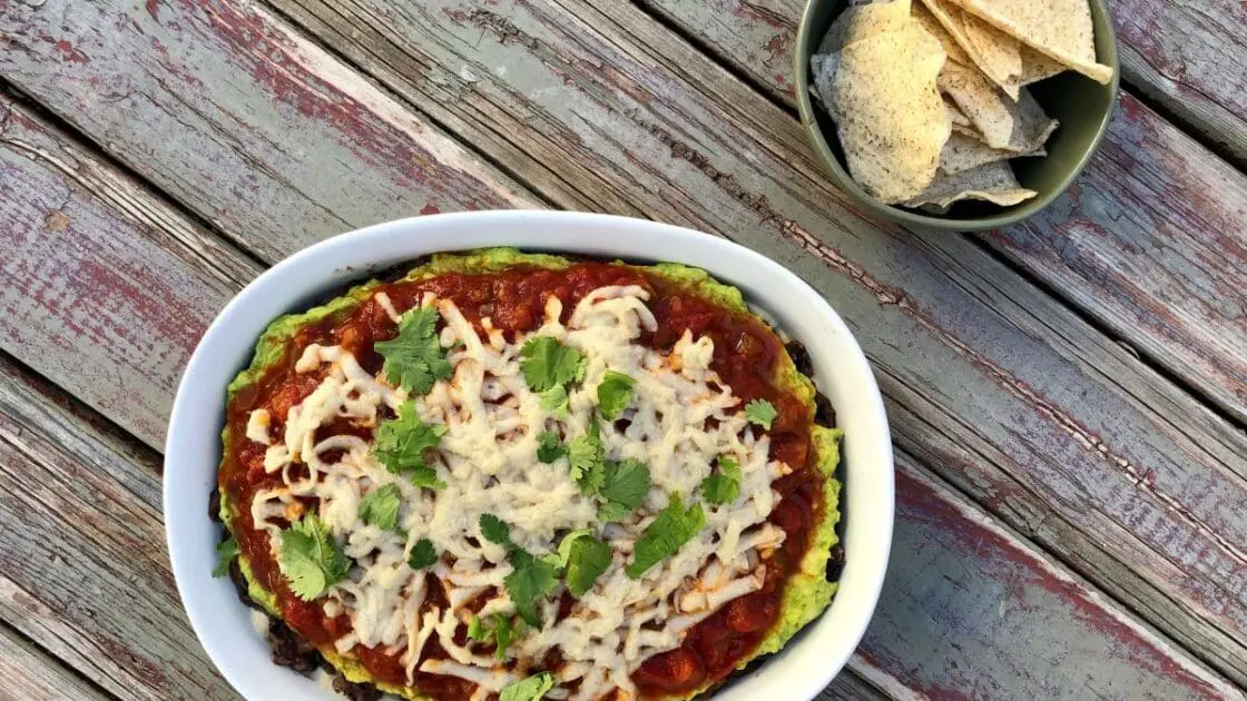 Image of healthy Vegetarian vegan 5 layer black ben dip on a table served with a small bowl of tortilla chips. It's the healthiest 5 layer bean dip ever via Organic Authority