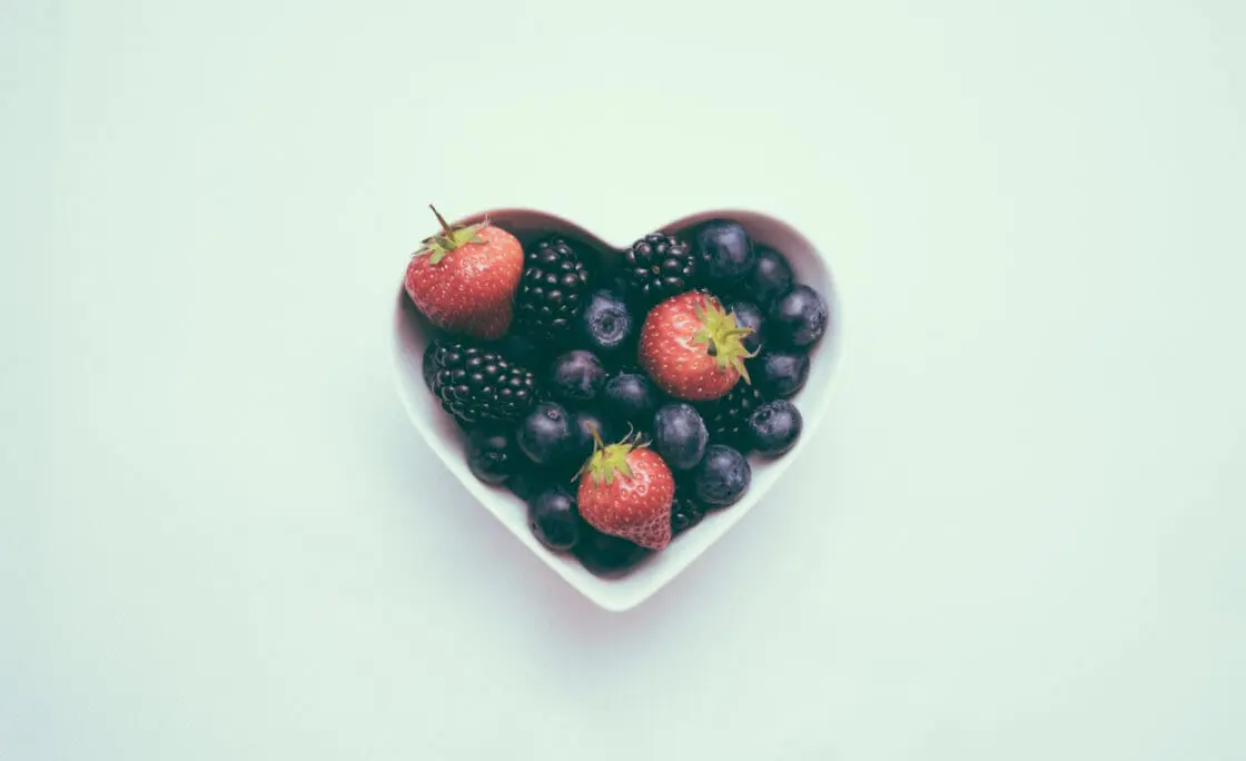 A heart-shaped bowl of berries that are on the blue foods list for foods for longevity via Organic Authority.
