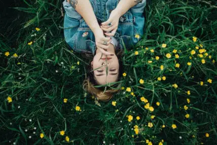 woman lying in green meadow surrounded by yellow flowers