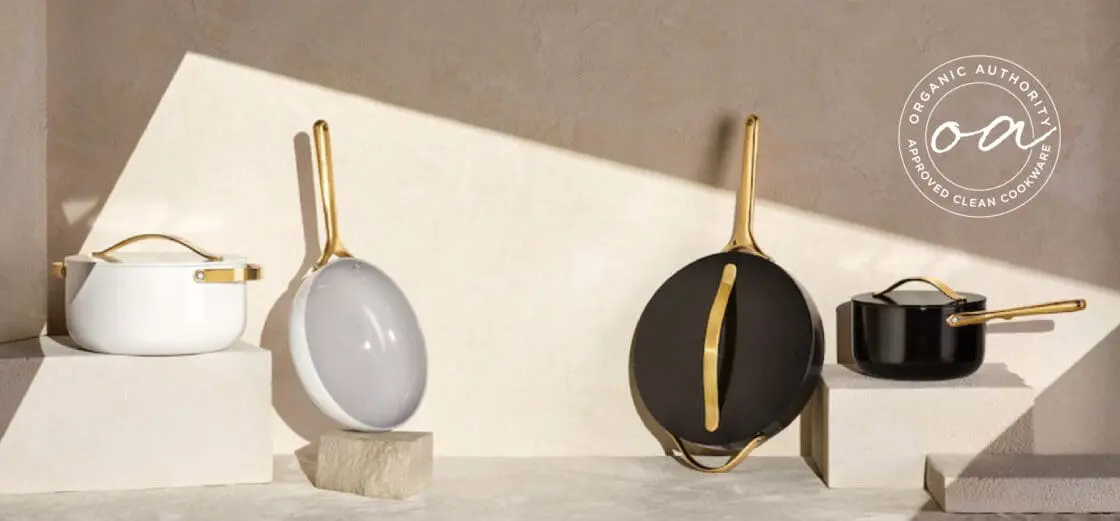 Image of Caraway cookware set, iconics black and white both with gold handles, on stone counter with textured beige wall with Organic Authority Approved Clean Cookware Seal