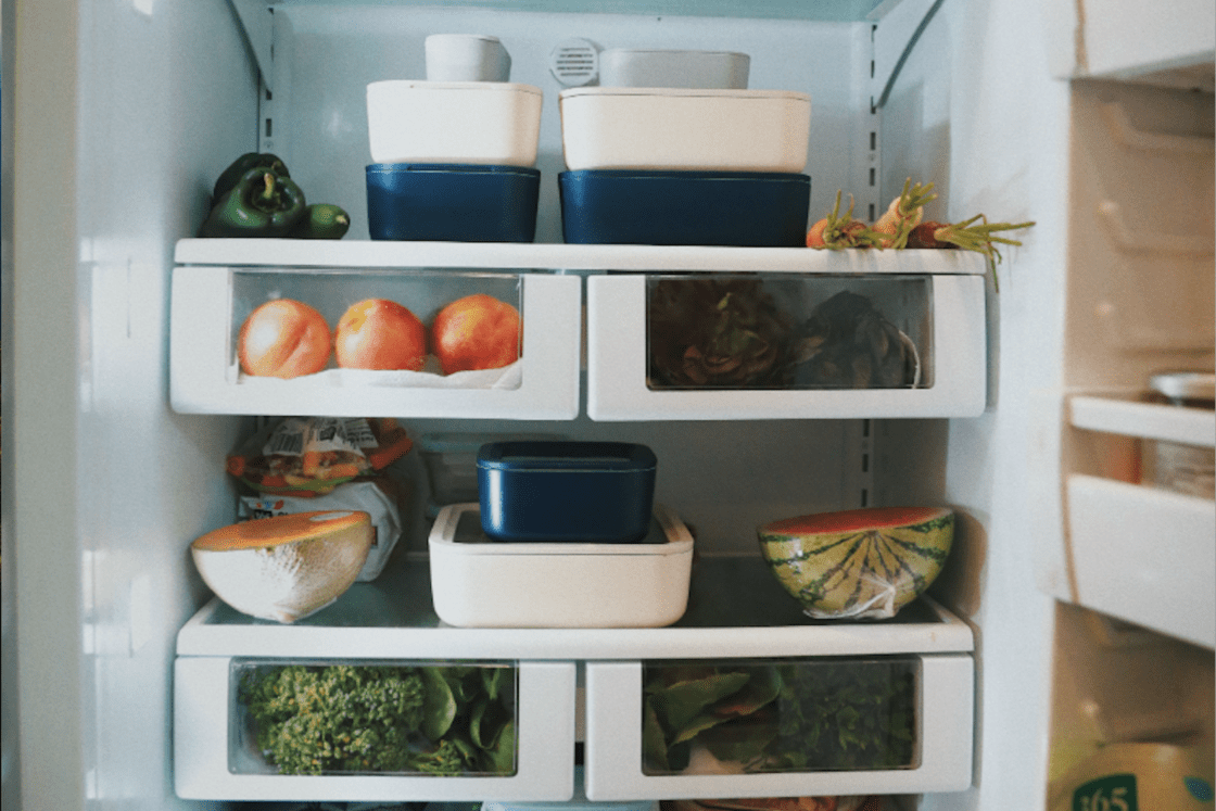 Image of Caraway Food Storage Containers in navy and cream in Laura Klein's refrigerator, two shelves shown with fresh greens, carrots, peppers, honeydew and watermelon