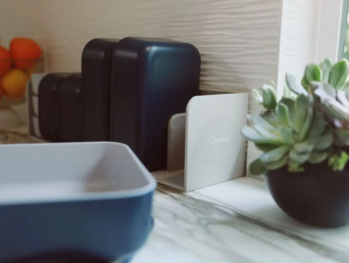 Image of Caraway Food Storage Containers in navy on Laura Klein's counter in the storage organizer alongside a succulent plant and a glass bowl of oranges.