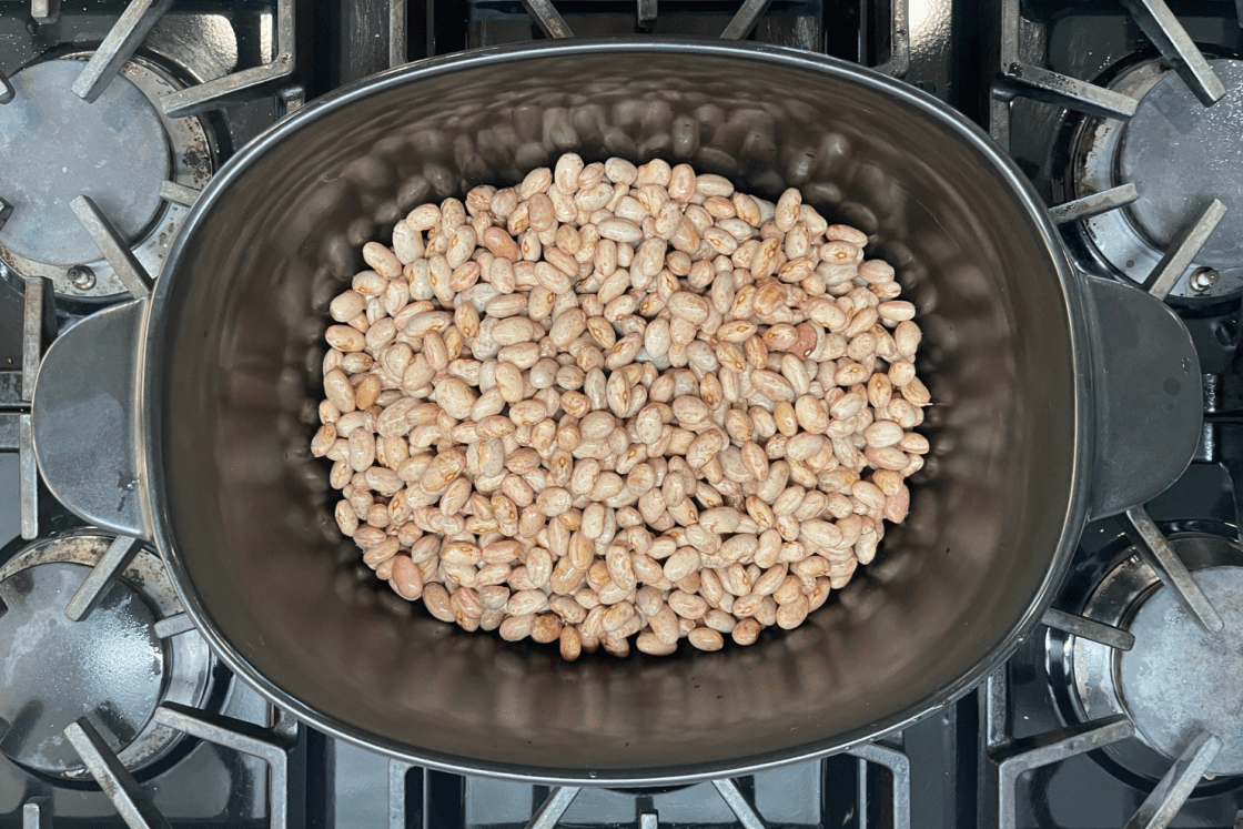 Image of dried beans in the bottom of a black, oval dutch oven made out of ceramic on the top of a gas range from an overhead view in a non-toxic kitchen. Xtrema is a premium safe cookware line.
