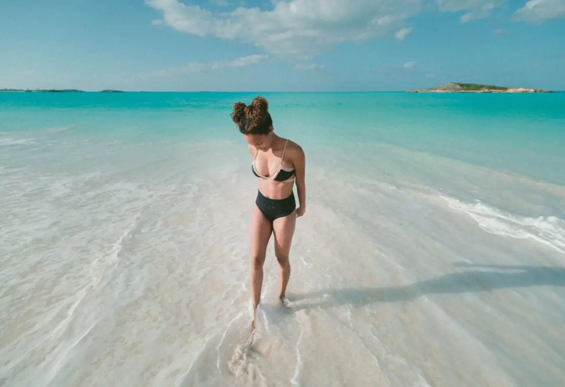 Woman wearing bikini standing in blue water considering marine collagen benefits.