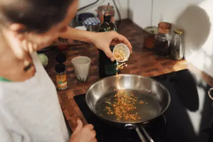 Woman pouring chopped garlic into saute pan.
