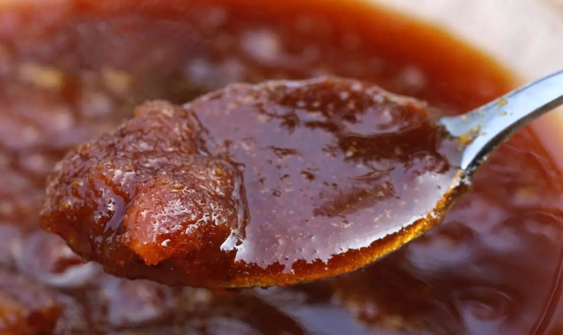 A spoonful of thick dark date molasses lifted from a bowl