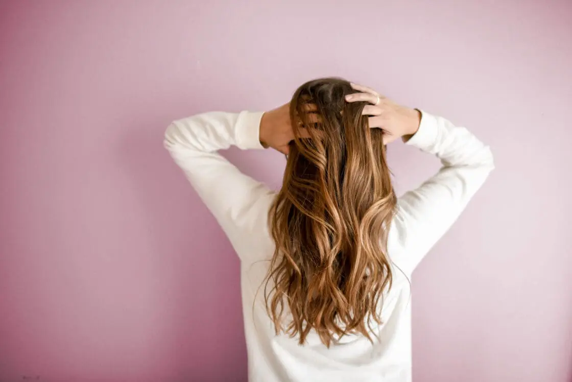 The back of a woman's head, hands in her long healthy hair, collagen powders help minimize signs of aging.