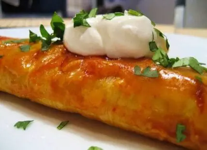 Image of an enchilada topped with homemade enchilada sauce and sour cream.