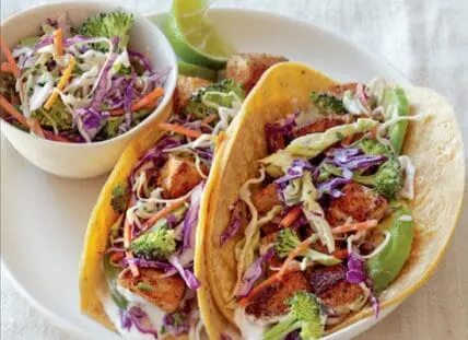 Image of two fish tacos with slaw made with broccoli and served with a tangy lime crema.