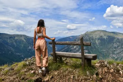 woman standing at top of mountain next to bench