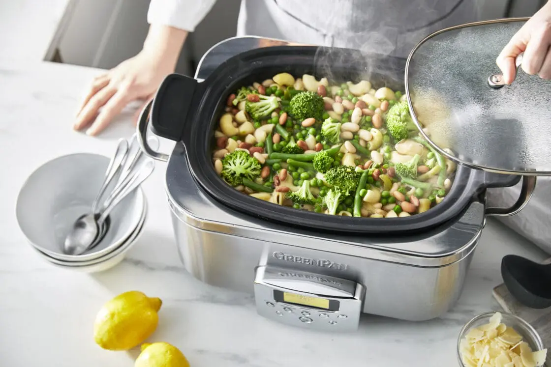 Image of chef standing behind the greenpan slow cooker filled with a grew stew of broccoli beans and more.