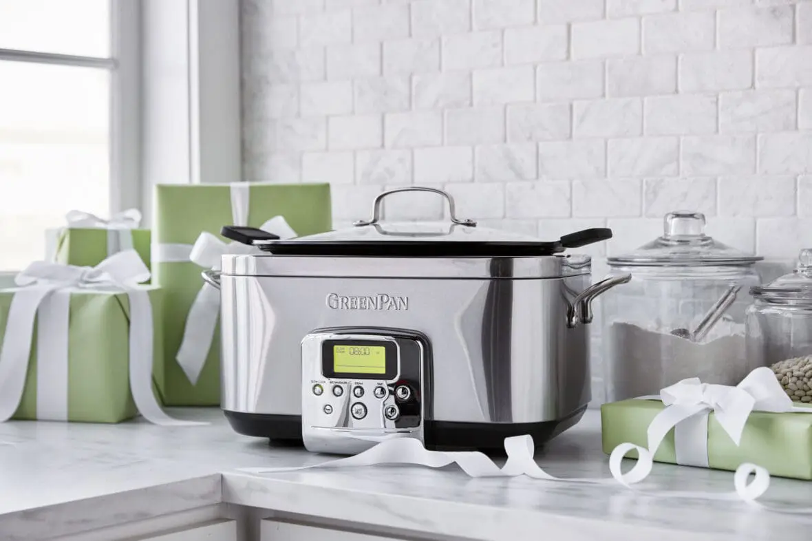 Image of GreenPan Slow Cooker on a white marble countertop with marble subway backsplash and a window. Also on the counter gifts wrapped in light green and tied with a white ribbon.