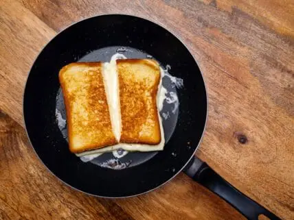 Image of grill cheese in a skillet on a table. This is the Absolute Guide to the Best Cheese for Grilled Cheese, Mac and Cheese, and Fondue