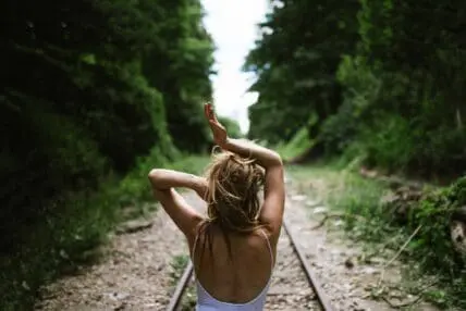woman in a forest on train track with hands in hair and above head