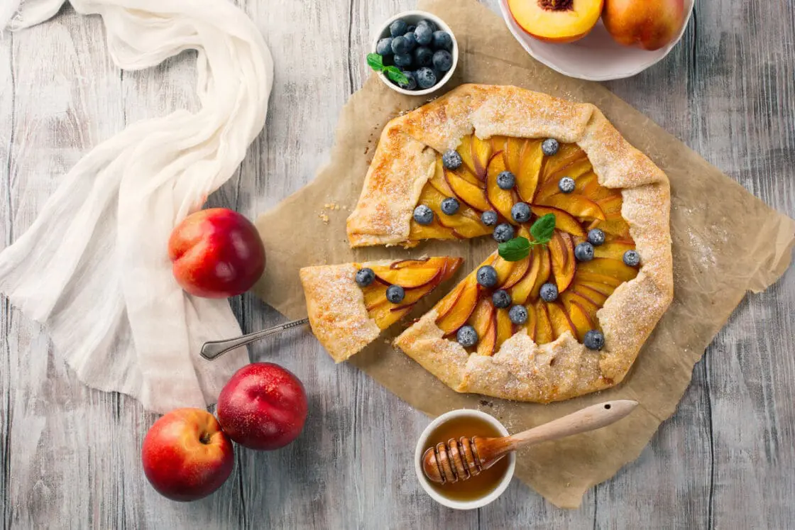 Homemade pie with peaches, ricotta and fresh blueberries on rustic white wooden background, top view