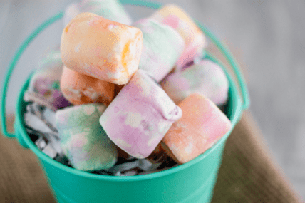 Image of colorfully dyed vegan marshmallows in a teal bucket. This invites you to learn how to dye marshmallows for Easter or for any fun holiday for which you want to add some color.