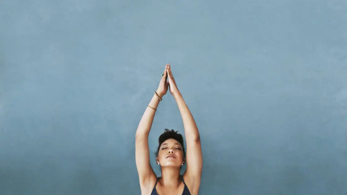 Image: woman with hands in arrow pose over her head wearing blue yoga top. How to Take Your Yoga Practice To New Heights with These 3 Breathing Techniques