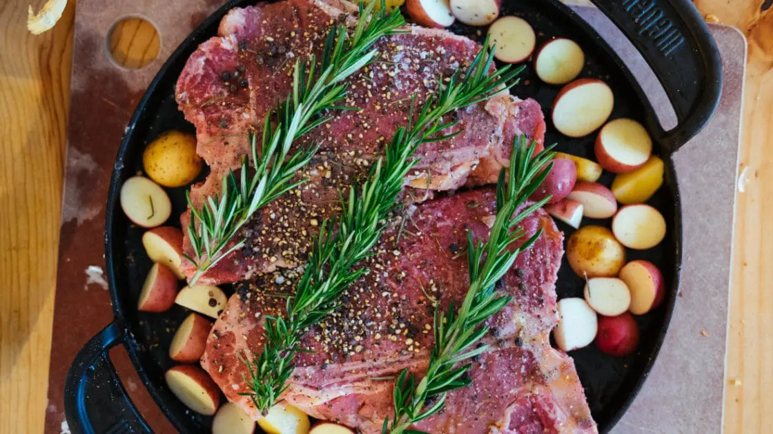 porterhouse steaks on grill pan with potatoes and rosemary